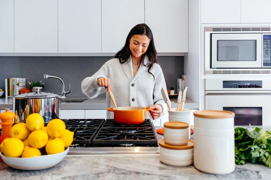 Woman cooking in a modern kitchen with fresh ingredients and organized kitchenware, smiling while stirring a pot